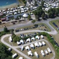 stellplatz_ferienpark Ein großer Parkplatz vor einem Ferienpark, mit geparkten Wohnmobilen und Blick auf einen See im Hintergrund.