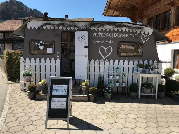The «Alpen-Charme» caravan in summer A caravan converted into a shop on a forecourt