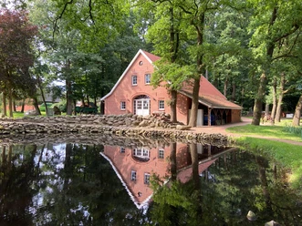 Heimathaus Börger Backsteingebäude mit rotem Ziegeldach am Teichufer, umgeben von alten Bäumen und Natur.