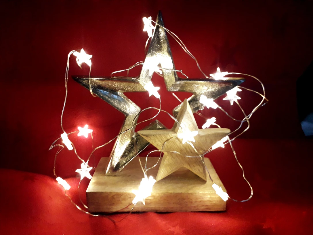 Sternstunde Zwei goldene Sterne, von sternförmigen Lichterketten umhüllt, auf rotem Hintergrund platziert.