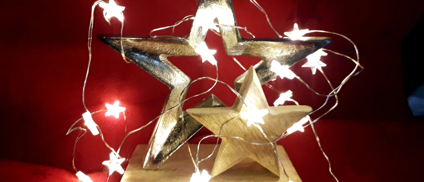 Zwei goldene Sterne, von sternförmigen Lichterketten umhüllt, auf rotem Hintergrund platziert.