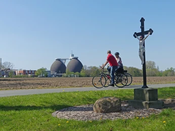 Zwei Radfahrer passieren einen Weg, im Hintergrund Faultürme der Paderborner Kläranlage.