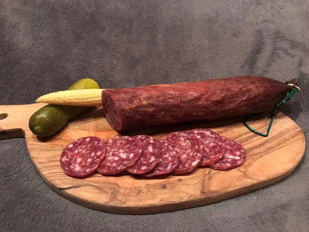 Saucisse sèche de bœuf fine Planche en bois avec une saucisse sèche de bœuf découpée, un cornichon et du maïs