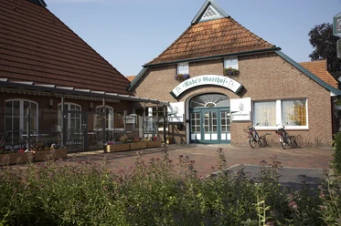 Rabes Gasthof Das Bild zeigt Rabes Gasthof aus rotem Backstein mit einem großen Eingang und einem Ziegeldach. Vor dem Gasthof stehen zwei Fahrräder.