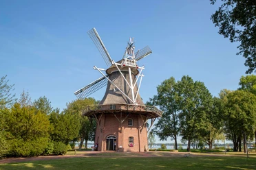 windmühle im kurpark Eine historische Windmühle im Kurpark, umgeben von grüner Natur und Bäumen, unter strahlend blauem Himmel.