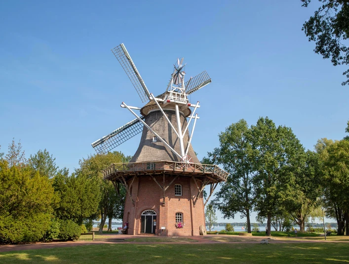 windmühle im kurpark Eine historische Windmühle im Kurpark, umgeben von grüner Natur und Bäumen, unter strahlend blauem Himmel.