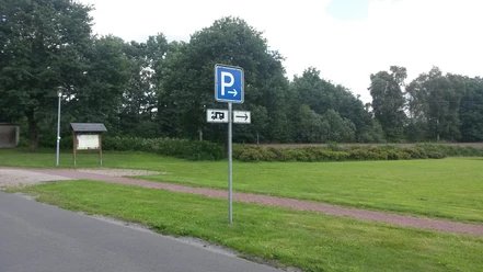 Wohnmobilstellplatz Hengstforde Das Bild zeigt einen Wohnmobilstellplatz, umgeben von grünen Wiesen und Bäumen. Ein Schild mit einem „P“ weist auf die Parkmöglichkeit hin und ein Weg führt durch die Landschaft.