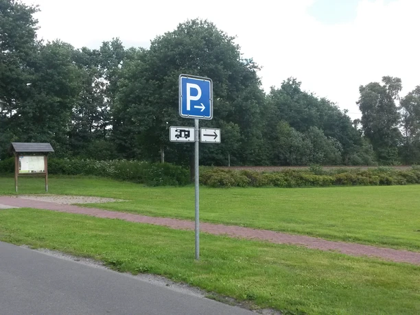 Wohnmobilstellplatz Hengstforde Das Bild zeigt einen Wohnmobilstellplatz, umgeben von grünen Wiesen und Bäumen. Ein Schild mit einem „P“ weist auf die Parkmöglichkeit hin und ein Weg führt durch die Landschaft.