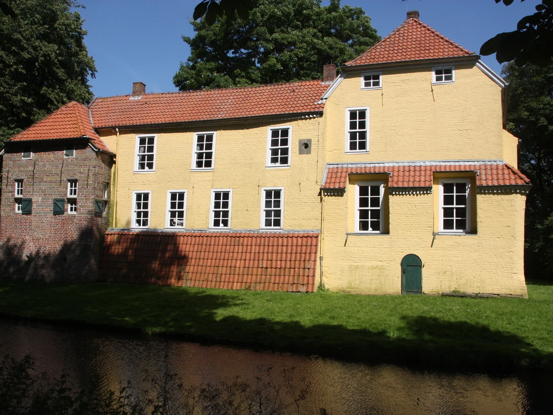 Manningaburg Pewsum Die historische Manningaburg in Pewsum mit gelber Fassade, rotem Dach und Wassergraben.
