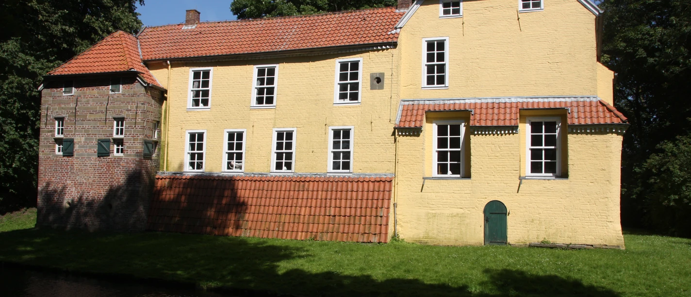 Manningaburg Pewsum Die historische Manningaburg in Pewsum mit gelber Fassade, rotem Dach und Wassergraben.
