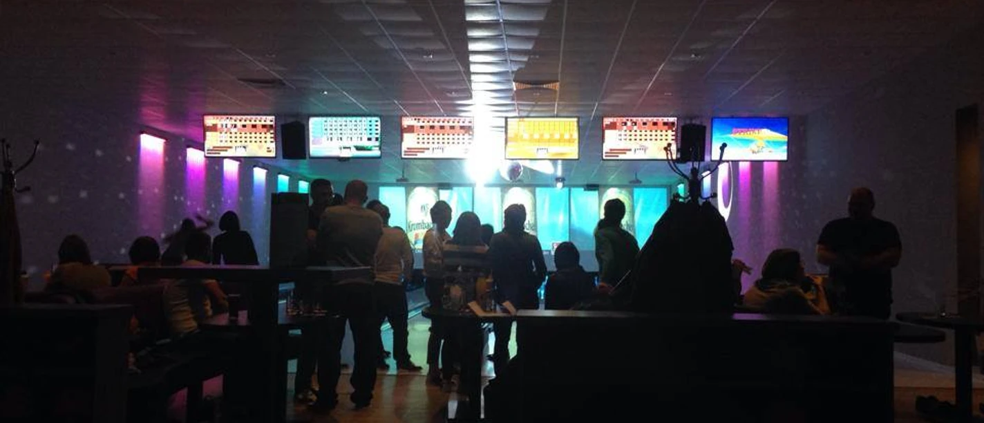 Bowlingcente Werlte Menschen beim Bowling in beleuchtetem Bowlingcenter mit Bildschirmen und farbigen Lichtern.