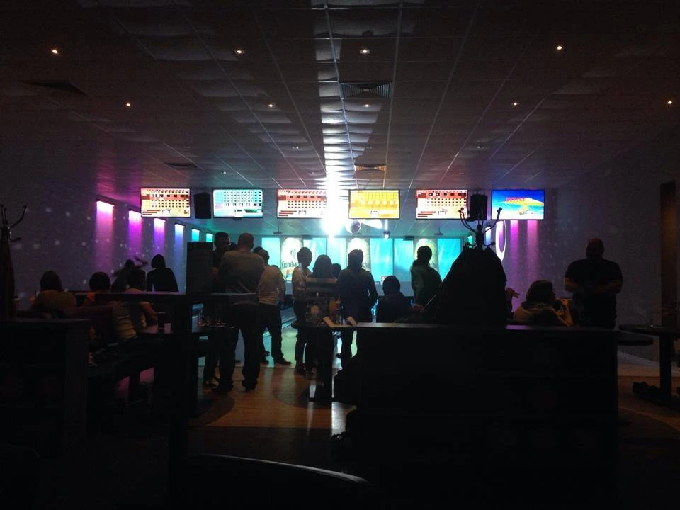 Bowlingcente Werlte Menschen beim Bowling in beleuchtetem Bowlingcenter mit Bildschirmen und farbigen Lichtern.