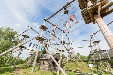 Kletterpark Snowworld Im Kletterpark balancieren drei Personen über hohe Seilbrücken zwischen mehreren Stationen.