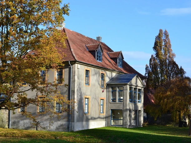Schloß "HAUS WERTHER" Historisches zweistöckiges Haus mit Erker, umgeben von herbstlichen Bäumen unter blauem Himmel.