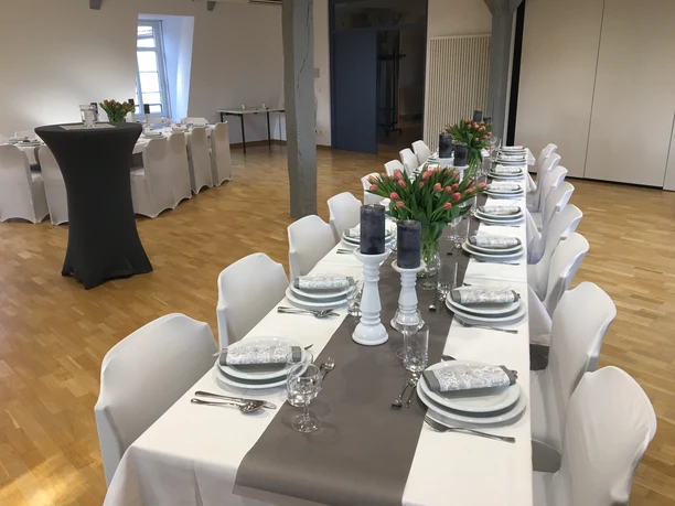 Elegant gedeckter Tisch in einem hellen Raum mit grauer Tischdecke, Blumen und Kerzen.