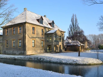 Bürgerbegegnungsstätte Haus Werther Historisches Gebäude mit schneebedecktem Dach, umgeben von einem zugefrorenen Wassergraben und Bäumen.