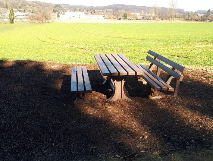 Holztisch mit zwei Bänken steht in ländlicher Umgebung, von Feldern und sanften Hügeln umgeben.