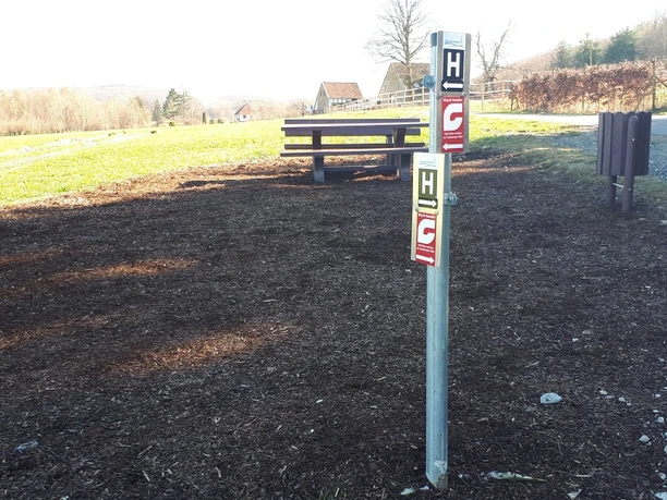 Rastplatz am Barenbergweg Ein ruhiger Rastplatz mit Holzbänken und einem Hinweisschild, umgeben von ländlicher Landschaft.