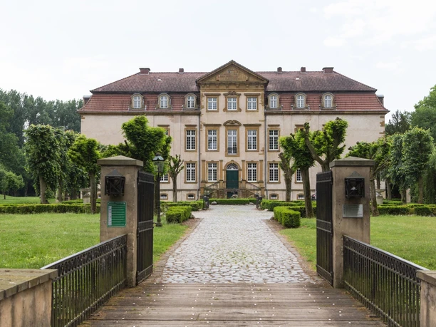 Historisches Herrenhaus mit symmetrischer Fassade, umgeben von gepflegtem Garten und Kiesweg.