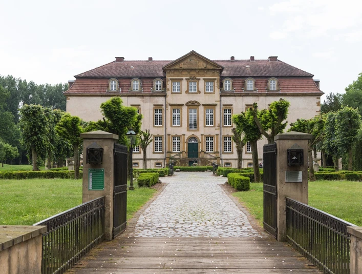 Historisches Herrenhaus mit symmetrischer Fassade, umgeben von gepflegtem Garten und Kiesweg.
