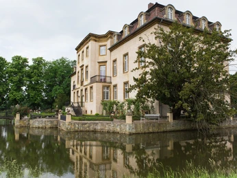 Schloss Möhler mit Teich Schloss mit klassischer Architektur, umgeben von einem ruhigen Wassergraben und grüner Vegetation.
