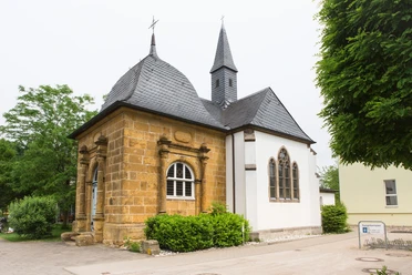 Die Loerdemann'sche Kapelle, ein Kleinod mitten in Herzebrock Kleine historische Kapelle mit schiefergedecktem Dach, flankiert von Bäumen und einem klaren Himmel.