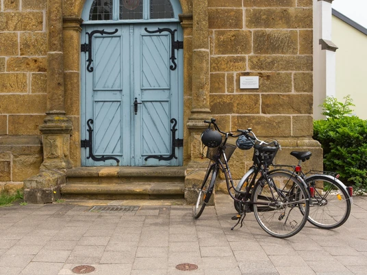 Zwei Fahrräder lehnen an einem historischen Sandsteingebäude mit blauer Doppeltür.