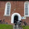 Evangelisch-reformierte Kirche Freepsum Backsteinkirche mit rundbogigem Eingang und geöffneter Tür, mehrere Fahrräder lehnen an der Wand.