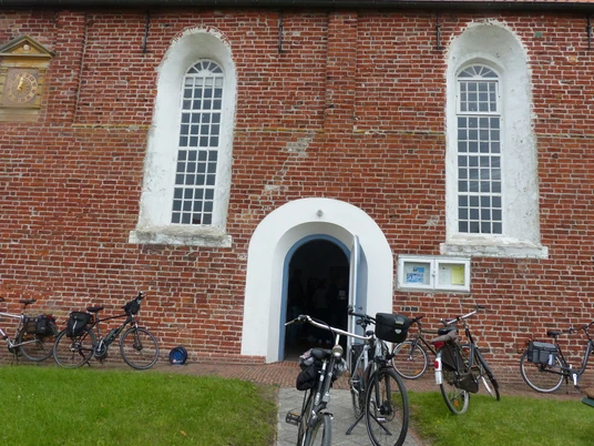 Evangelisch-reformierte Kirche Freepsum Backsteinkirche mit rundbogigem Eingang und geöffneter Tür, mehrere Fahrräder lehnen an der Wand.
