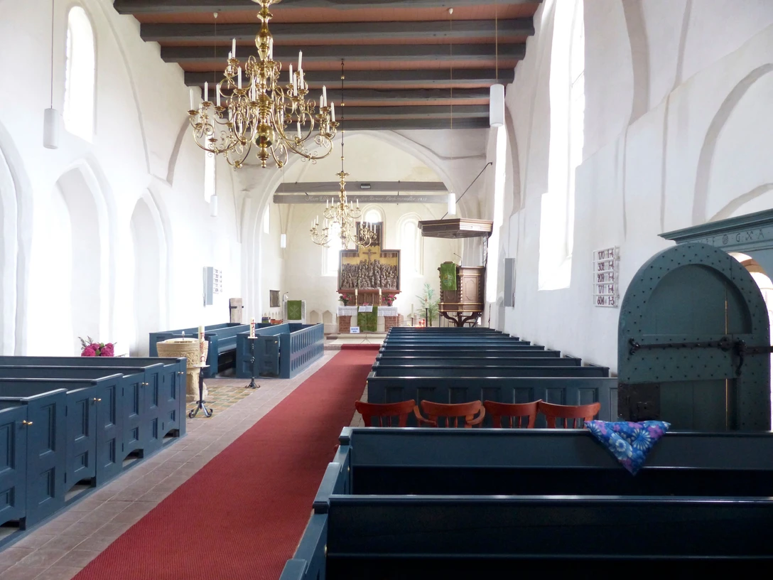 Ev.-ref. Kirche Loquard Innenraum der Kirche Loquard mit weißen Wänden, roten Teppichgängen, blauen Bänken und Altartisch.