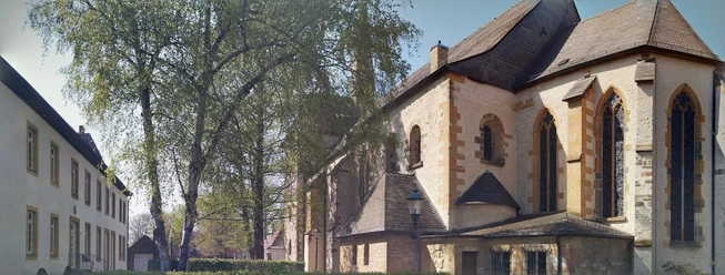 Pfarrkirche St. Laurentius, Clarholz am Kloster Historische Kirche mit romanischen Elementen neben belaubten Bäumen und angrenzenden Gebäuden.