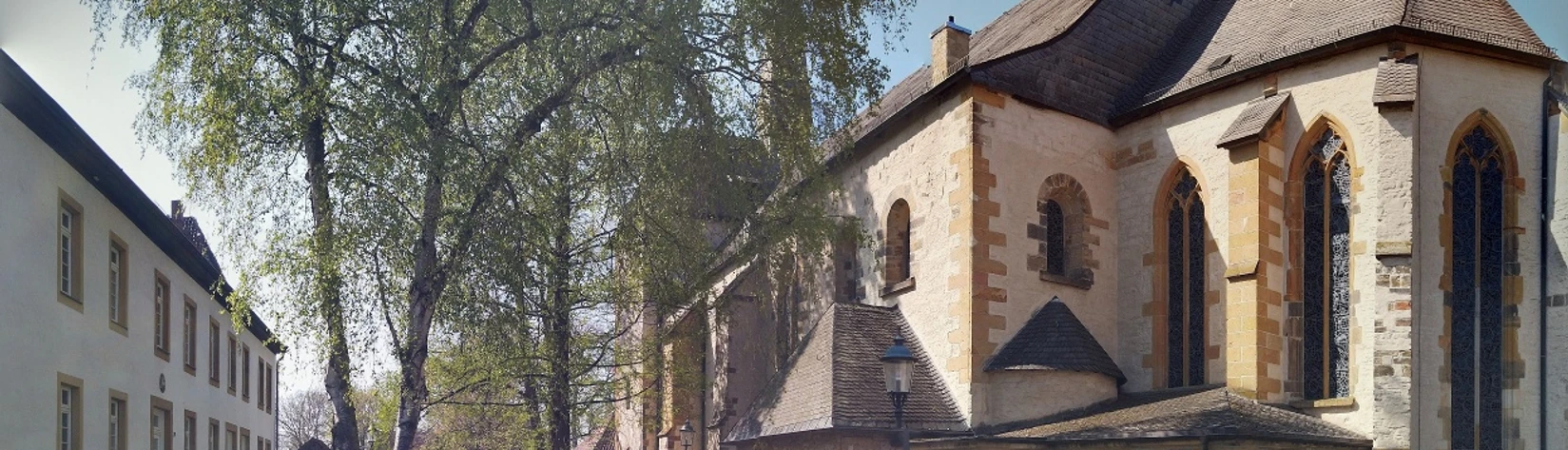 Pfarrkirche St. Laurentius, Clarholz am Kloster Historische Kirche mit romanischen Elementen neben belaubten Bäumen und angrenzenden Gebäuden.