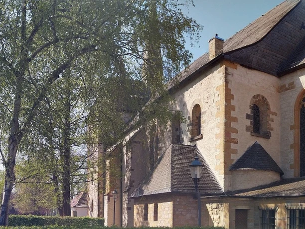 Pfarrkirche St. Laurentius, Clarholz am Kloster Historische Kirche mit romanischen Elementen neben belaubten Bäumen und angrenzenden Gebäuden.