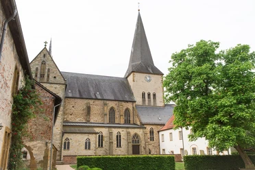 Pfarrkirche St. Christina in Herzebrock Historische Kirche mit hohem Turm und Uhr, umgeben von alten Gebäuden und grünem Baum.