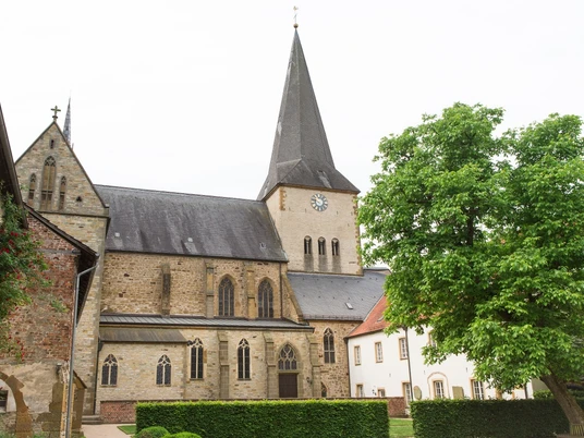 Pfarrkirche St. Christina in Herzebrock Historische Kirche mit hohem Turm und Uhr, umgeben von alten Gebäuden und grünem Baum.