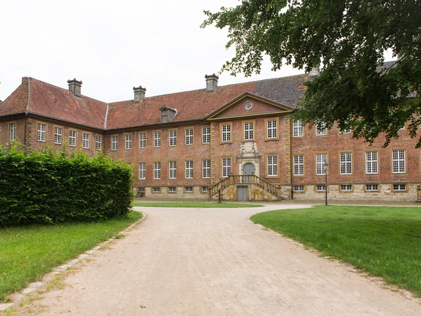 Backsteinernes Herrenhaus mit roten Ziegeln, symmetrische Fassade, vor einem gepflegten Gartenweg.
