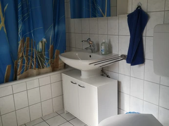 Badezimmer mit blauen Vorhängen, weißen Fliesen, Waschtisch und WC, ausgestattet für Funktionalität.