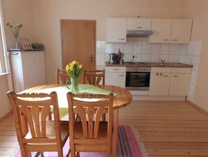 Küche, FeWo Krauß Helle Wohnküche mit Holztisch und vier Stühlen, ausgestattet mit moderner Einbauküche und Kochutensilien.