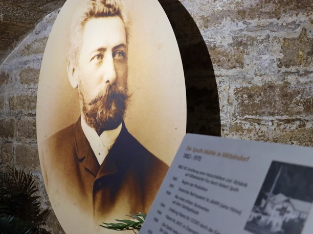 Ausstellung zur Sputh Mühle Ein sepiafarbenes Porträt eines Mannes mit Bart und Anzug vor einer Steinmauer; daneben eine Infotafel über die Spath-Mühle.