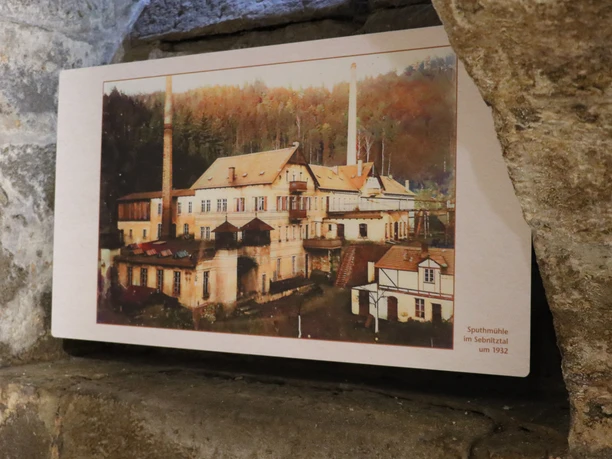 Historisch beeld van de Sputhmühle molen in de Sebnitz vallei rond 1932, omgeven door bos, met een opvallende schoorsteen en gebouw met meerdere verdiepingen.