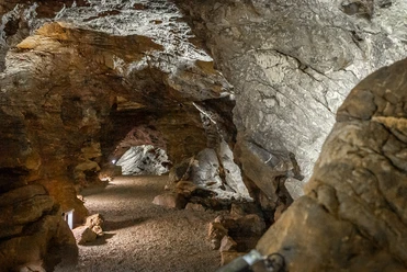 Aggertalhöhle Steinige Höhle mit beleuchtetem, gewundenem Pfad. Wände aus braunen und grauen Felsen mit Textur.