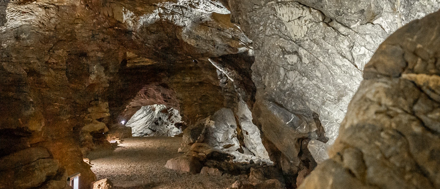 Aggertalhöhle Steinige Höhle mit beleuchtetem, gewundenem Pfad. Wände aus braunen und grauen Felsen mit Textur.