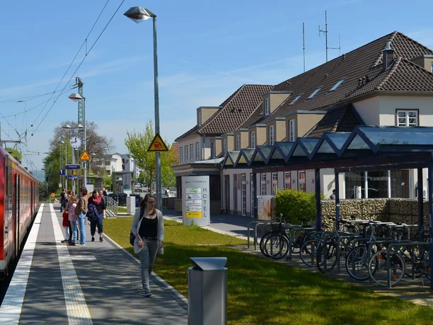 Eine rote S-Bahn hält am Bahnsteig des modernen Bahnhofs Steinheim mit Radabstellplatz und Reisenden.