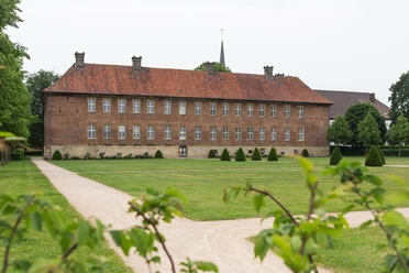 Ziegelstein-Herrenhaus mit Satteldach auf grüner Wiese, umrahmt von Bäumen und gepflegten Wegen.