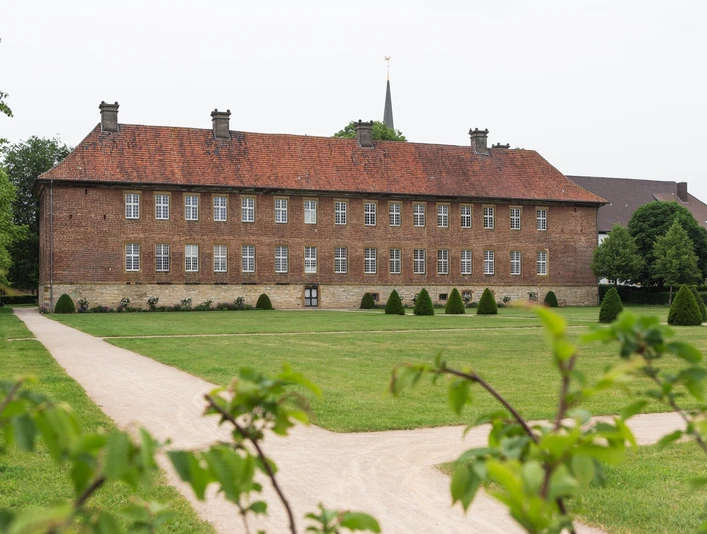 Klosteranlage Clarholz vom Garten aus gesehen Ziegelstein-Herrenhaus mit Satteldach auf grüner Wiese, umrahmt von Bäumen und gepflegten Wegen.