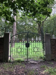 Jüdischer Friedhof Historischer jüdischer Friedhof mit schwarzem Eisentor, verzierten Davidsternen und grünem Baumhintergrund.