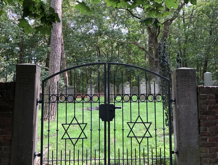 Jüdischer Friedhof Historischer jüdischer Friedhof mit schwarzem Eisentor, verzierten Davidsternen und grünem Baumhintergrund.
