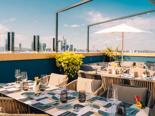 Frankfurt Blasky Rooftop Gepflegter Tisch mit Gläsern auf Dachterrasse mit Skyline im Hintergrund.