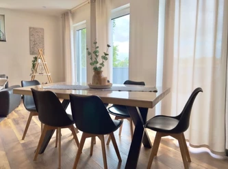 Esszimmer Ferienwohnung Well-Being Esszimmer mit Holzfußboden, modernem Tisch, sechs Stühlen und großen Fenstern mit viel Tageslicht.