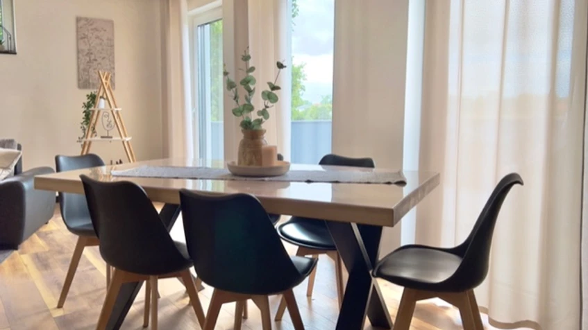 Esszimmer Ferienwohnung Well-Being Esszimmer mit Holzfußboden, modernem Tisch, sechs Stühlen und großen Fenstern mit viel Tageslicht.